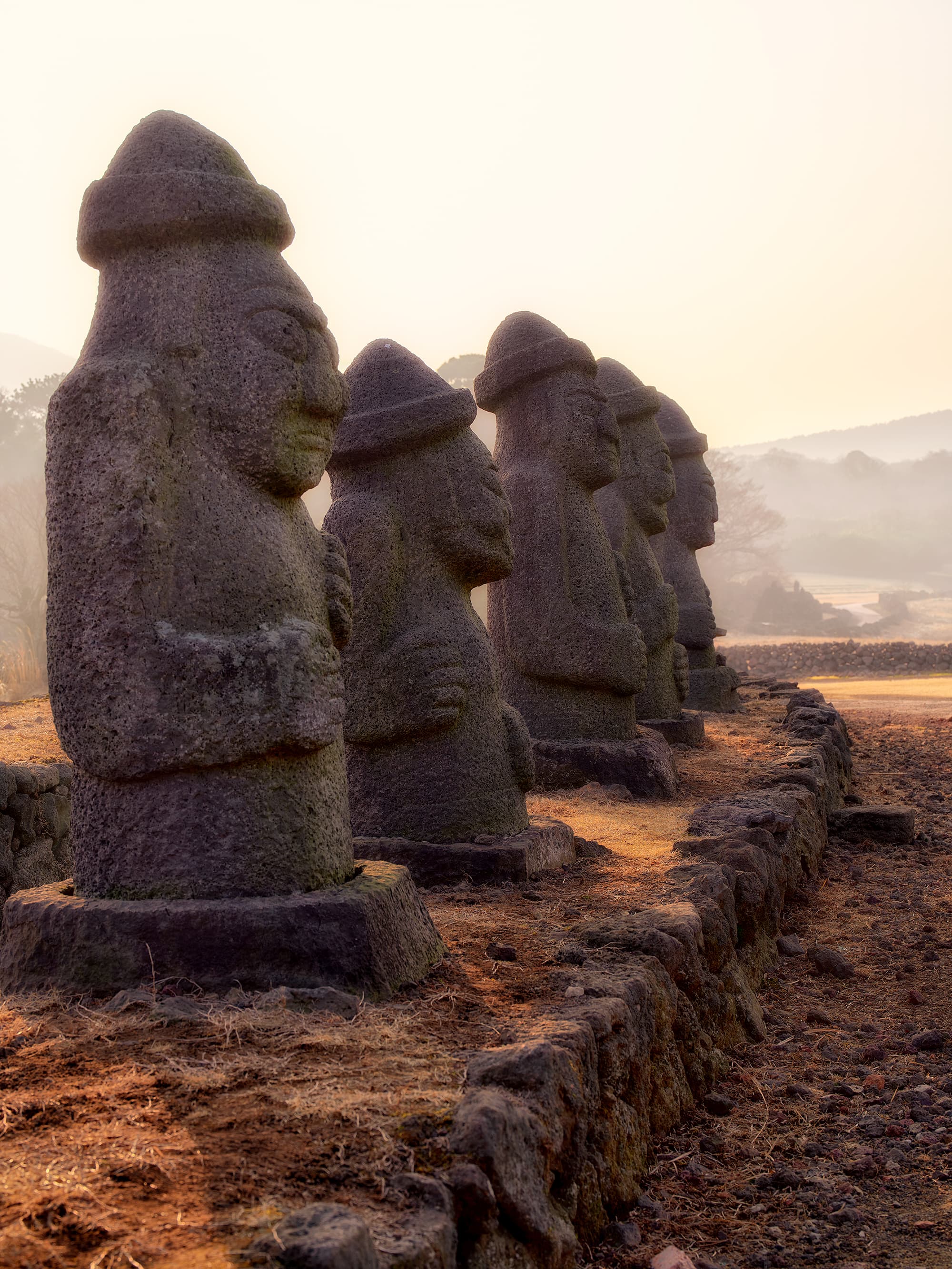 Line of Dolharubang statues in golden misty backlight