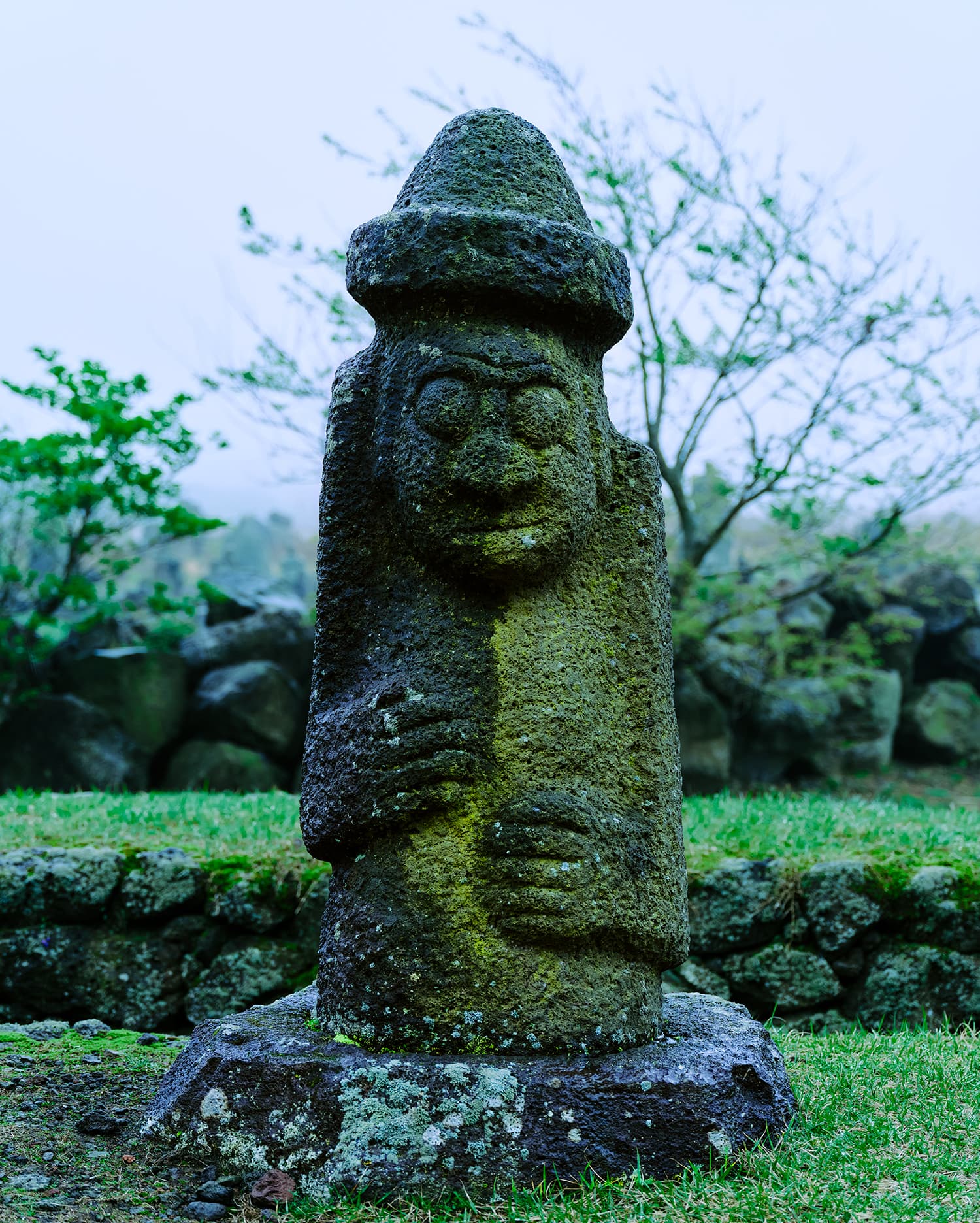 Tall Dolharubang statue with pointed hat against trees