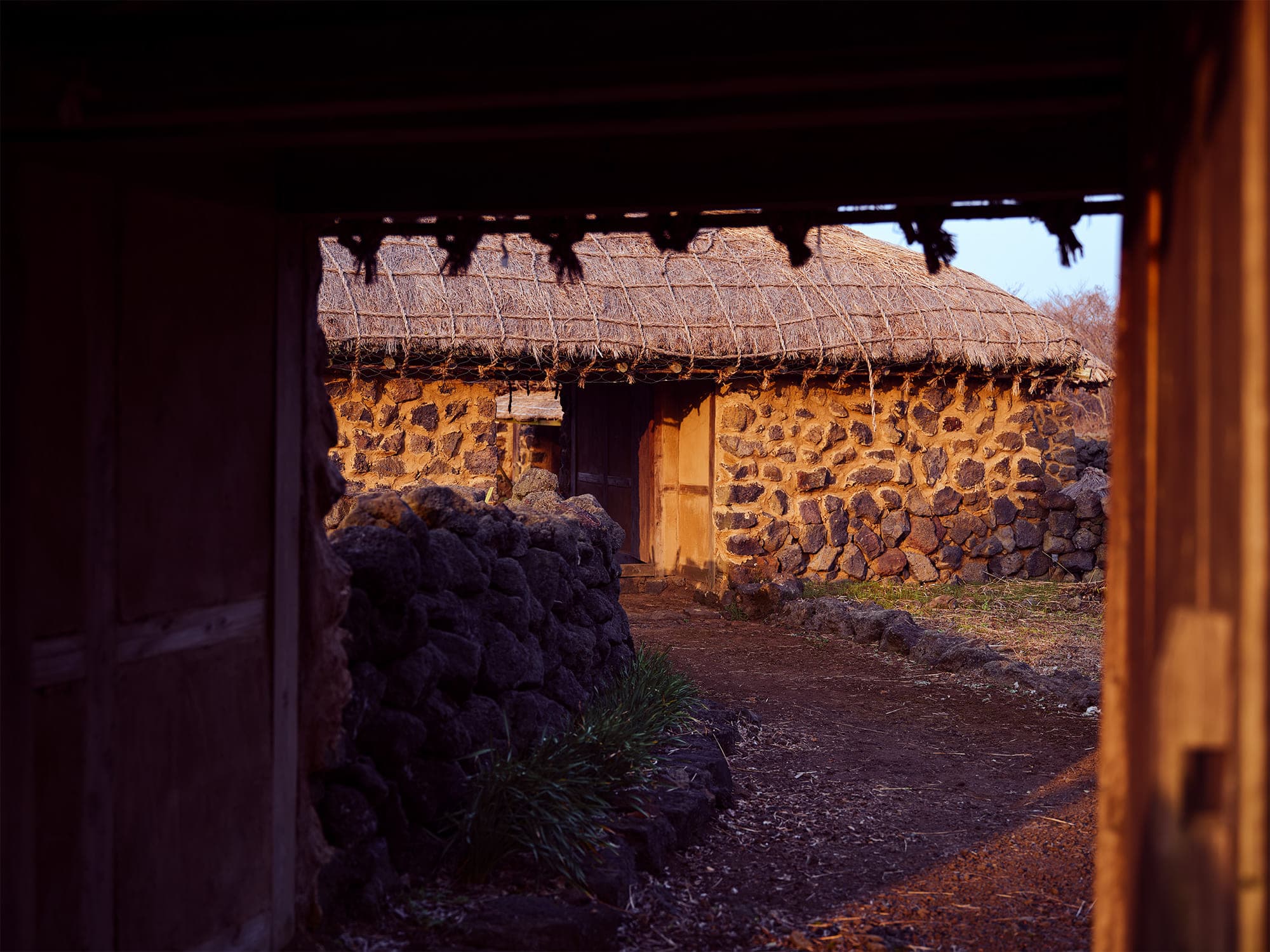 View through a dark doorway to a sunlit thatched stone house